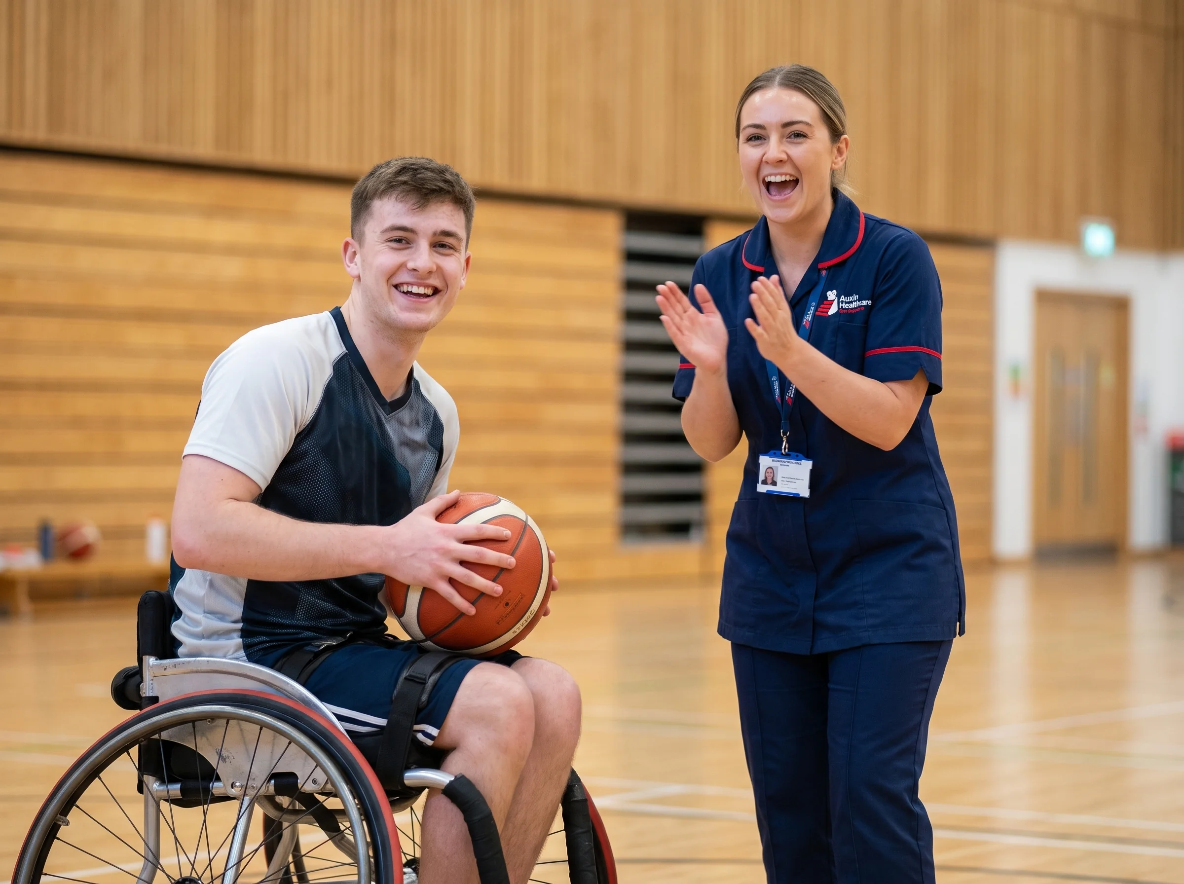 Young man playing wheelchair basketball, cheered on by an Auxin support worker at a Lincolnshire sports centre